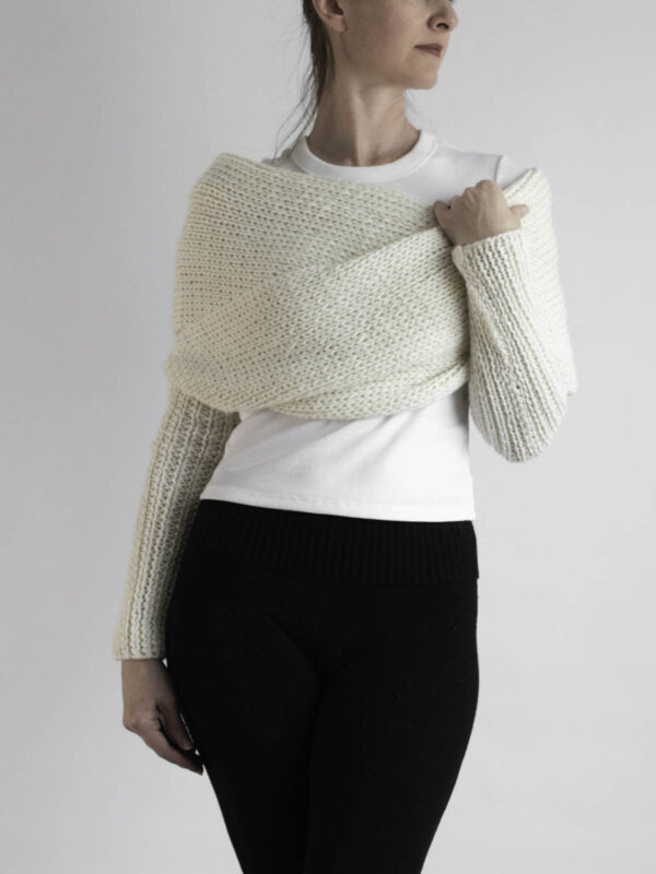 Cream knit sweater scarf worn over a white tee with long ribbed sleeves, styled with black pants