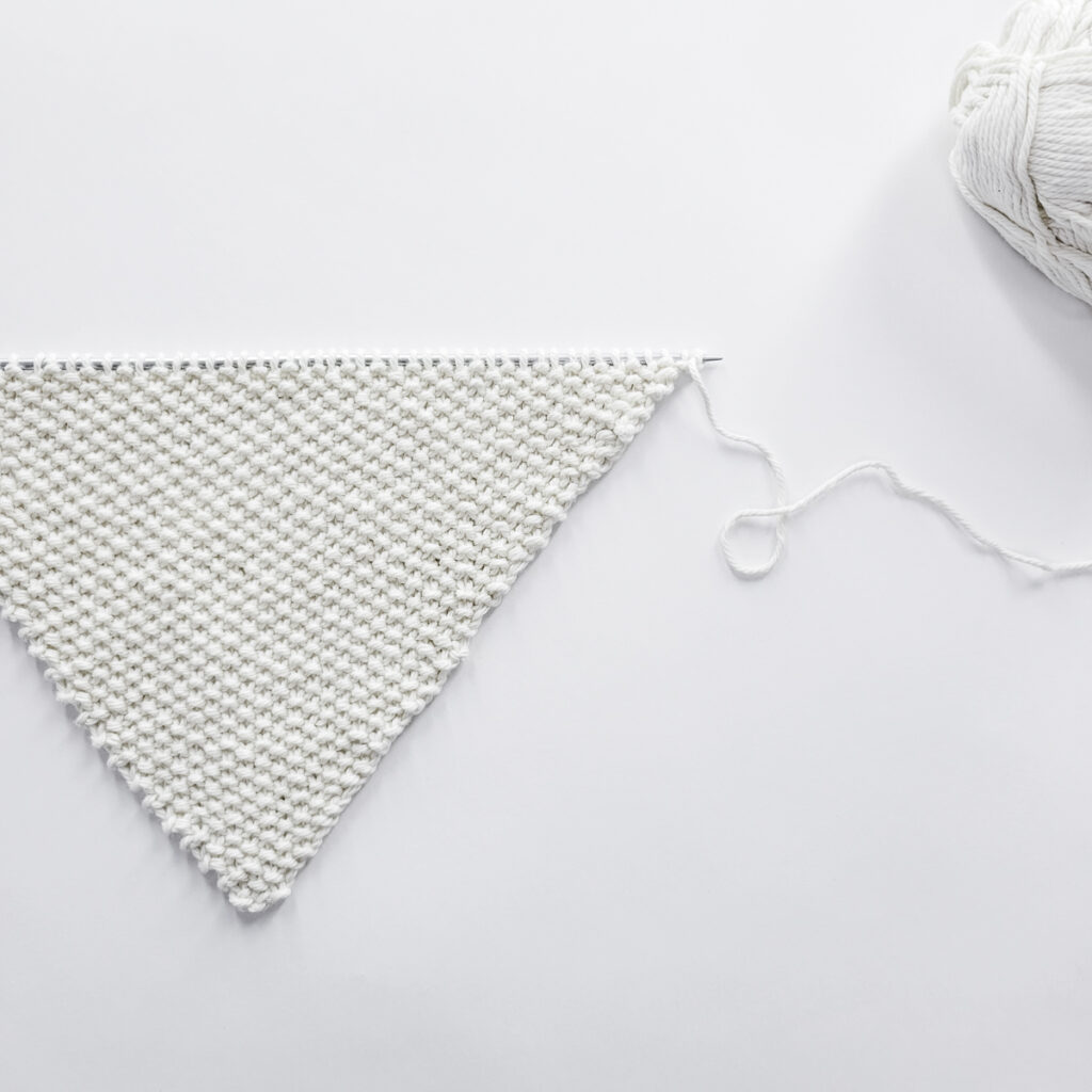 pic of a corner-to-corner dishcloth half knitted, on a knitting needle