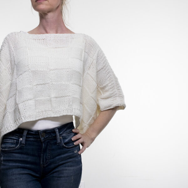 A woman showcasing a seamless checkerboard stitch knitting pattern knit on a lightweight seamless poncho using DK weight yarn.