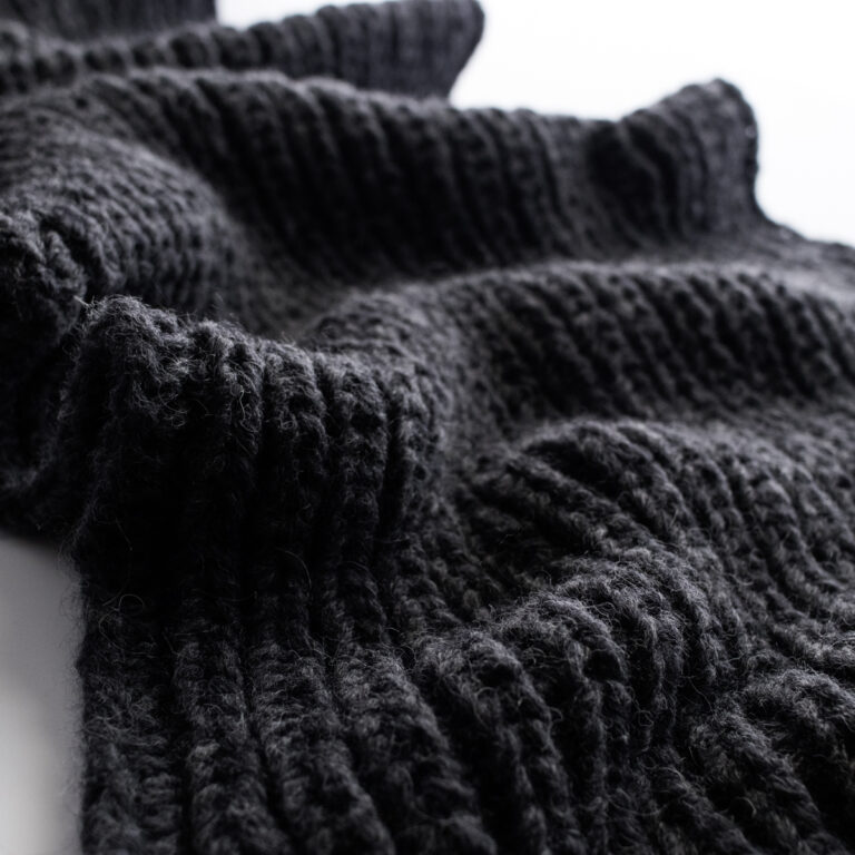 Close-up of the Misty Dewdrop Blanket in soft black bulky yarn, showing the squishy fisherman rib texture and airy stitch definition.