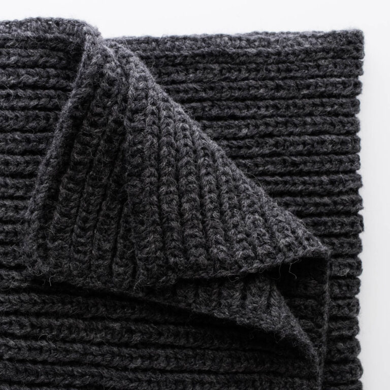 Folded Misty Dewdrop Blanket in bulky black yarn, showcasing the thick fisherman rib stitch pattern and clean edging.