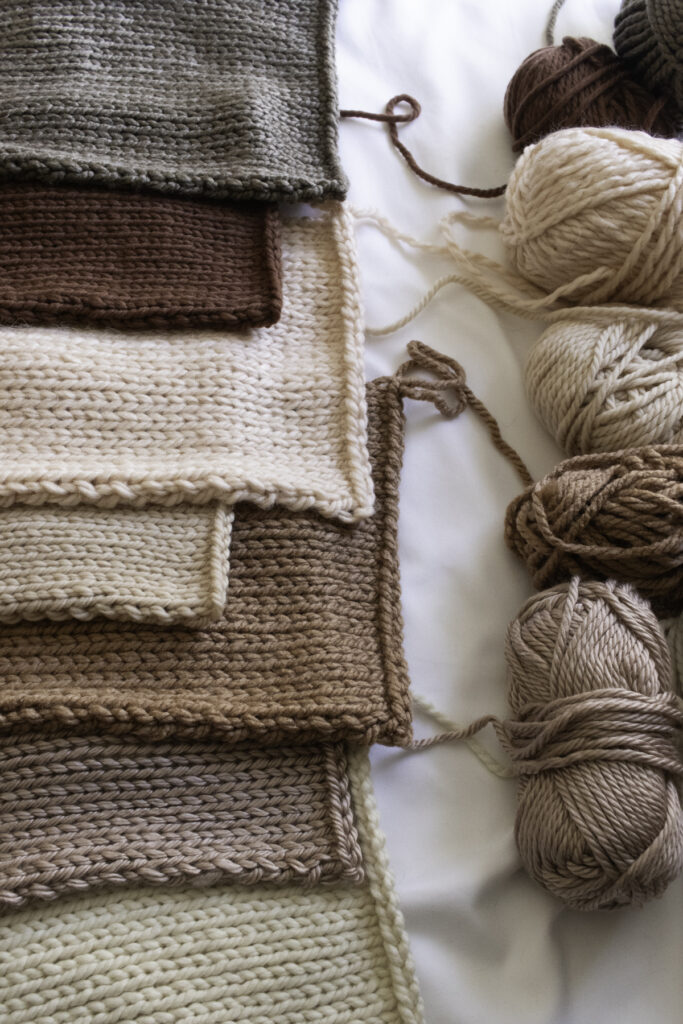 Flat lay of multiple knit swatches worked in super bulky yarns in natural, neutral tones with coordinating skeins above — ideal for comparing texture, thickness, and stitch definition between yarn brands.