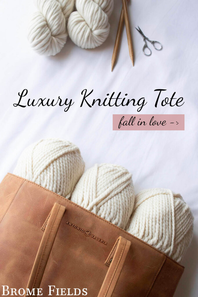 Overhead photo of a leather knitting tote filled with three skeins of white bulky yarn and knitting needles, surrounded by extra yarn and scissors.