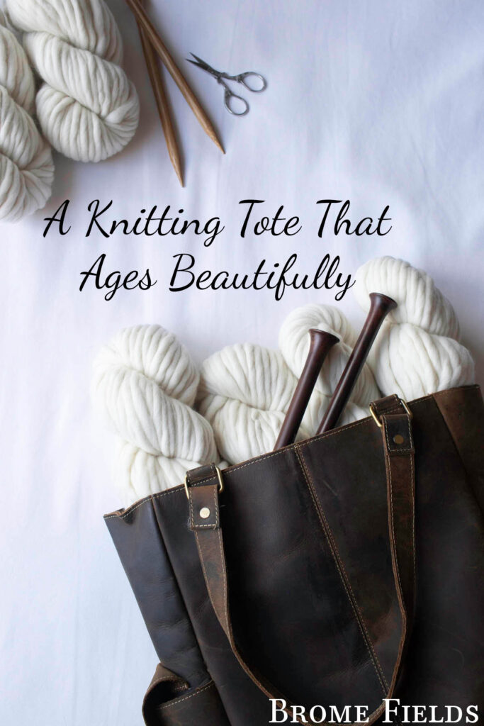 Top-down photo of a rustic leather tote stuffed with chunky cream yarn and knitting needles, with extra yarn and scissors placed nearby on a white background.