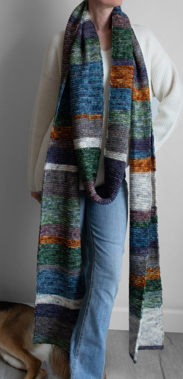 Woman wearing an extra long colorful striped garter stitch scarf in hand-dyed multicolor yarn, draped around her neck.