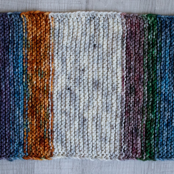 Close-up photo of a worsted yarn swatch in the garter stitch pattern. The back featuring alternating colors overlapping when switching. The yarn is soft colorful, showing clear stitch definition and beautiful squishy texture.