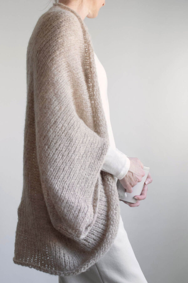 Side view of the oversized brushed alpaca shrug draped over shoulders, open front knit cardigan style worn with cozy cream joggers & tee.