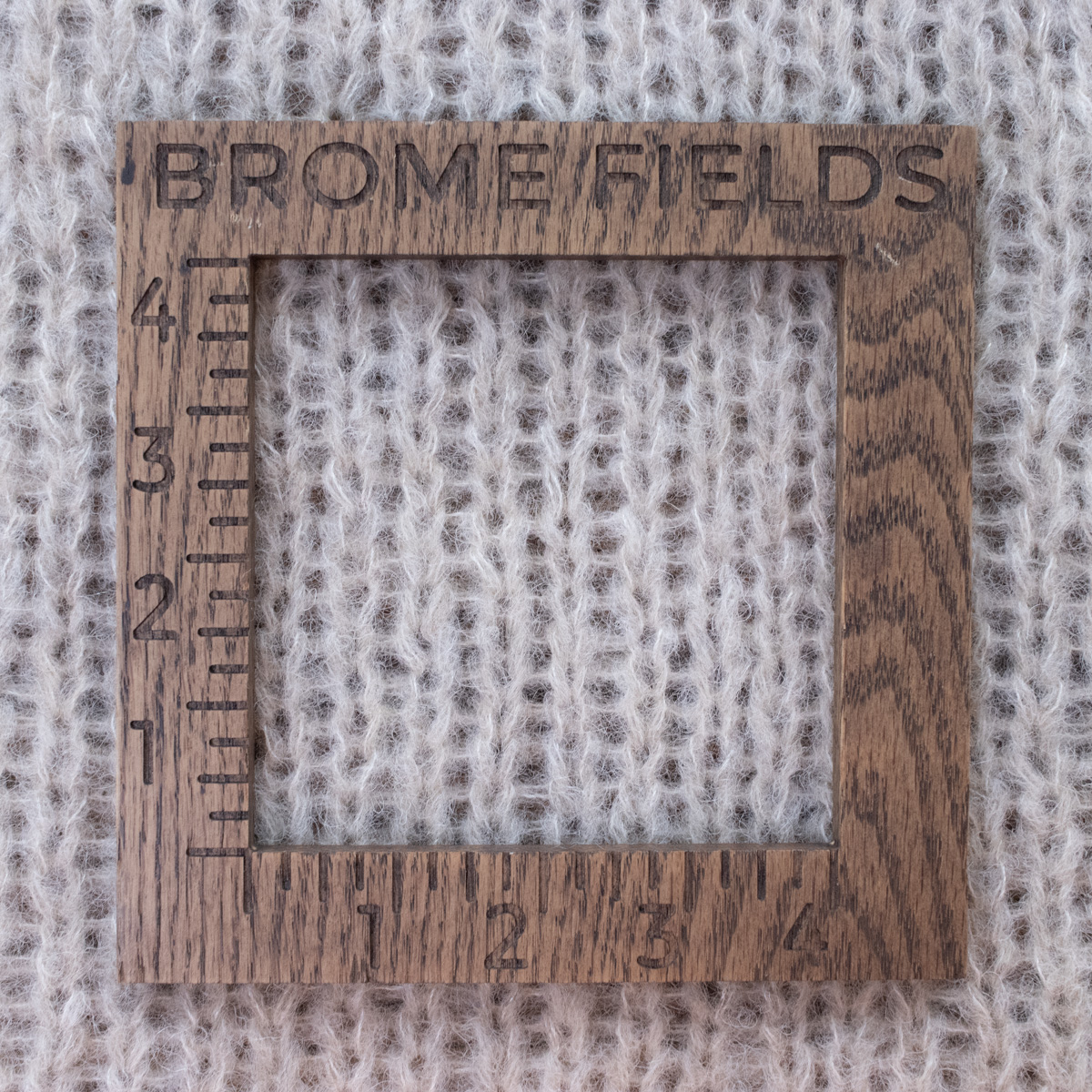 Close-up photo of a mohair yarn swatch in the garter stitch pattern, measured with a wooden 4-inch gauge ruler engraved with “Brome Fields.” The yarn is soft, showing clear stitch definition and beautiful squishy texture.