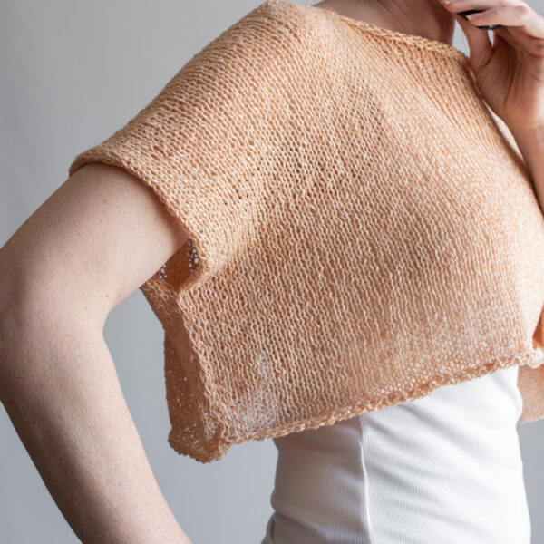 a woman wearing a peach linen knit tee from the front, back, and sides. The boxy cropped top has short sleeves and a wide neckline.