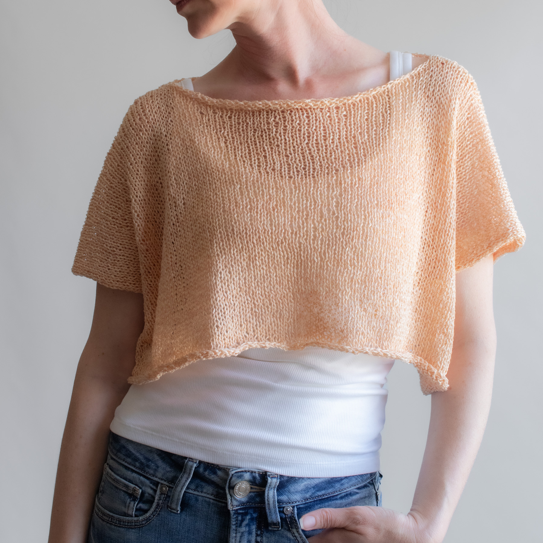 a woman wearing a peach linen knit tee from the front, back, and sides. The boxy cropped top has short sleeves and a wide neckline.