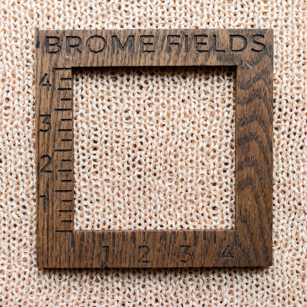 Close-up photo of a linen yarn swatch in the stockinette stitch pattern, measured with a wooden 4-inch gauge ruler engraved with “Brome Fields.”