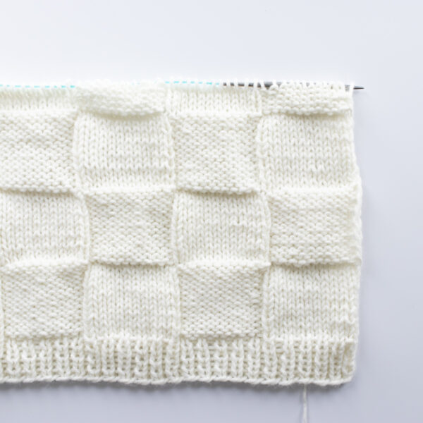 Handknit seamless quilt checkerboard knit blanket laying on a white background