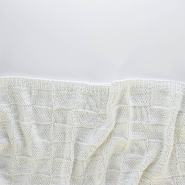 Handknit seamless quilt checkerboard knit blanket laying on a white background