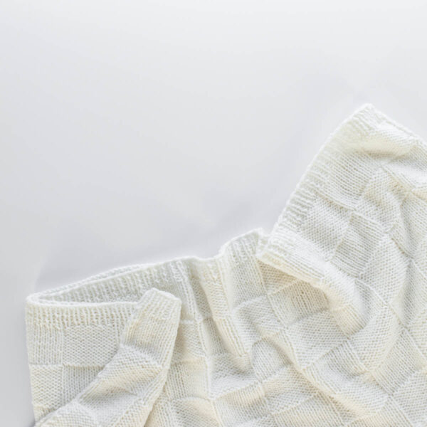 Handknit seamless quilt checkerboard knit blanket laying on a white background