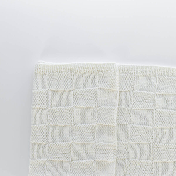 Handknit seamless quilt checkerboard knit blanket laying on a white background