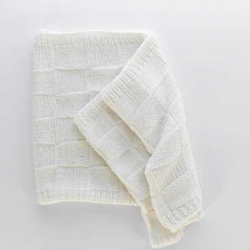 Handknit seamless quilt checkerboard knit blanket laying on a white background