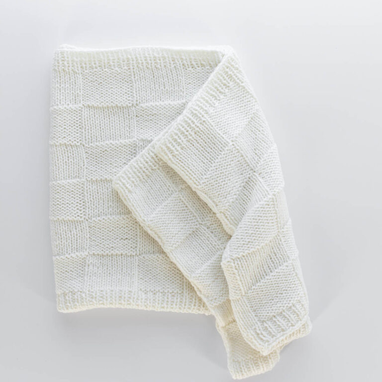 Handknit seamless quilt checkerboard knit blanket laying on a white background