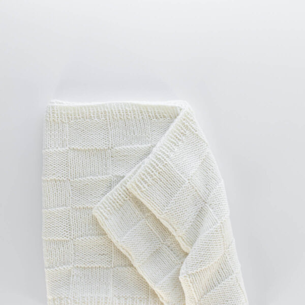Handknit seamless quilt checkerboard knit blanket laying on a white background