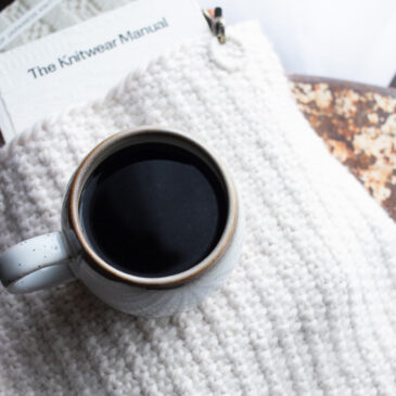 Pic of a linen stitch tote bag with books peeking out of the top sitting on a vintage metal chair with a cup of coffee on top