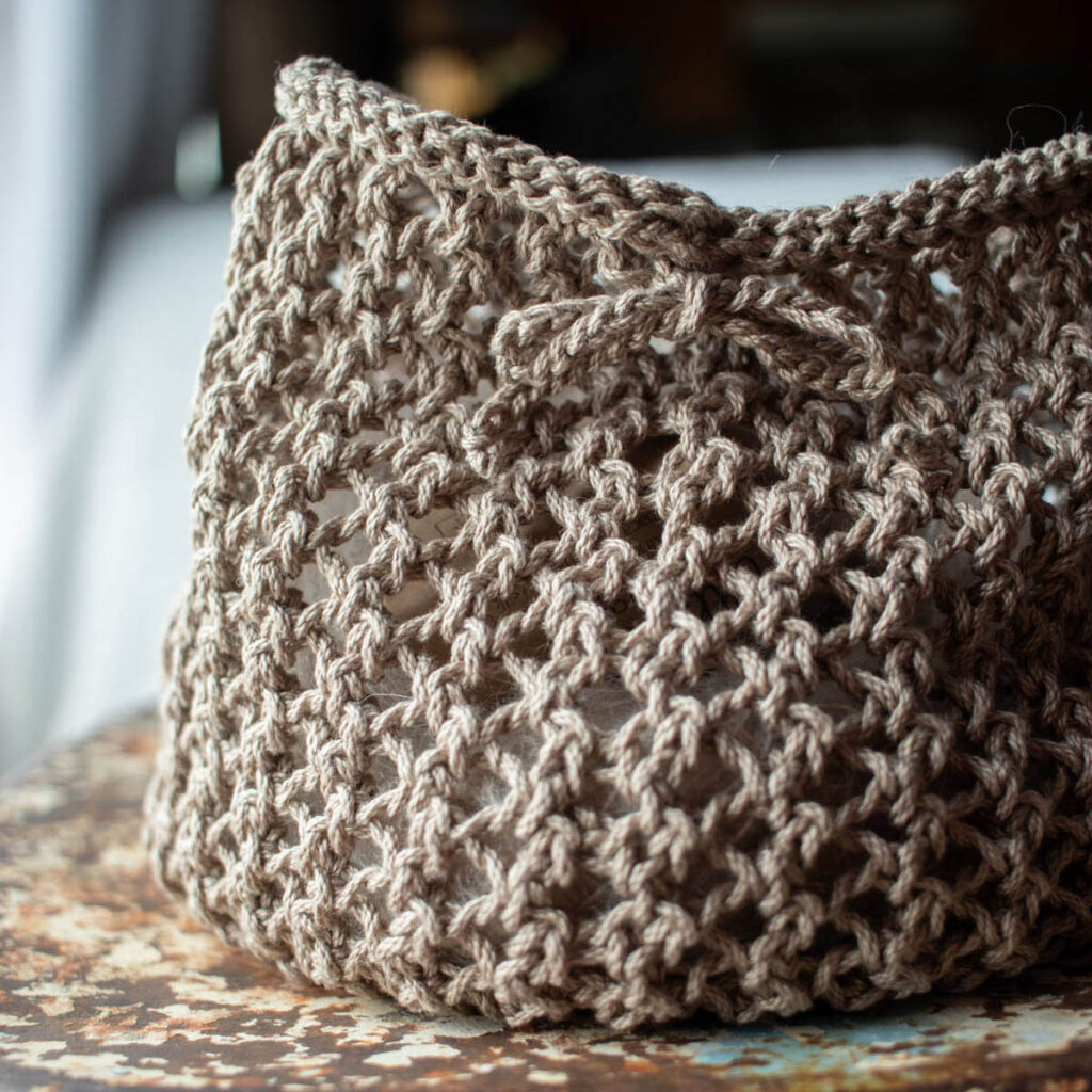 Close-up detail of a knit lace mesh bag with a crocheted chain drawstring tied in a bow.