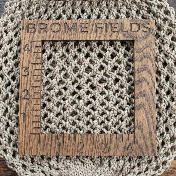 Close-up detail of a knit lace mesh bag, measured with a wooden 4-inch gauge ruler engraved with “Brome Fields.”