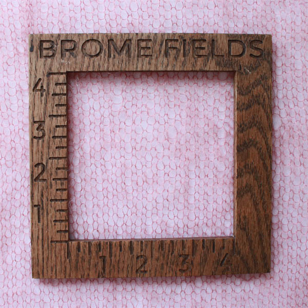 Close-up detail of a knit lace mohair scarf, measured with a wooden 4-inch gauge ruler engraved with “Brome Fields.”