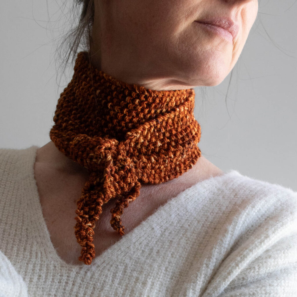 Close-up of a hand-dyed seed stitch skinny scarf tied in a kerchief knot