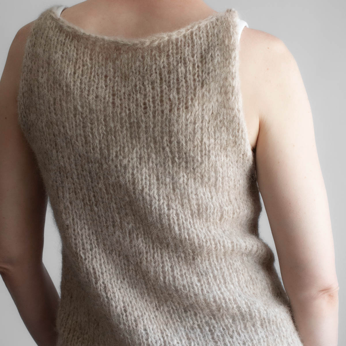 A model wearing a handknitted brushed alpaca tank top in oatmeal, shown from the back angle.